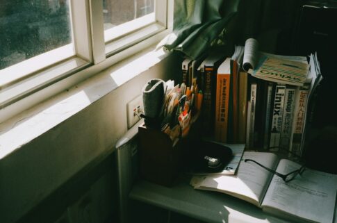窓辺の机に置かれた本と眼鏡を写したイメージ写真。有栖川有栖本人の写真ではありません
